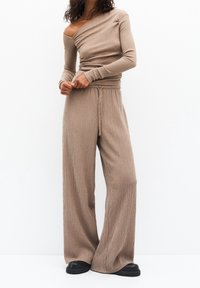 Haut marron en maille côtelée avec une épaule dénudée et des manches longues, associé à un pantalon à jambes larges. Tissu texturé avec un détail de ceinture à cordon.