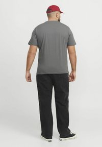 Grå t-shirt med korte ærmer og almindelig pasform, parret med sorte denimbukser og sorte sneakers. Kappen er rød med en buet skygge.