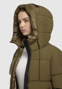 Olive zelený pufový kabát s veľkou, izolovanou kapucňou. Obsahuje čierny zips a nastaviteľné šnúrky. Hladká, lesklá textúra látky.