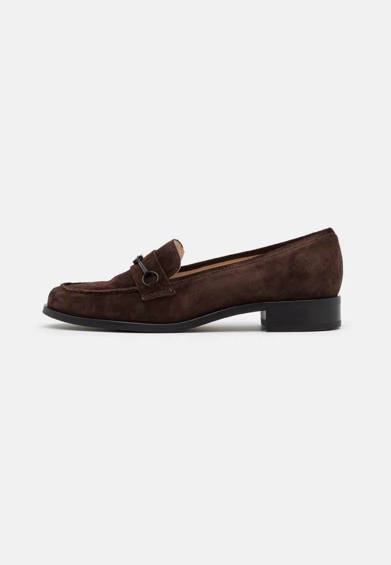 Mocassin en suède brun avec un talon carré bas, doté d'une bride décorative et d'un accent métallique. Texture lisse, design classique et bout arrondi.