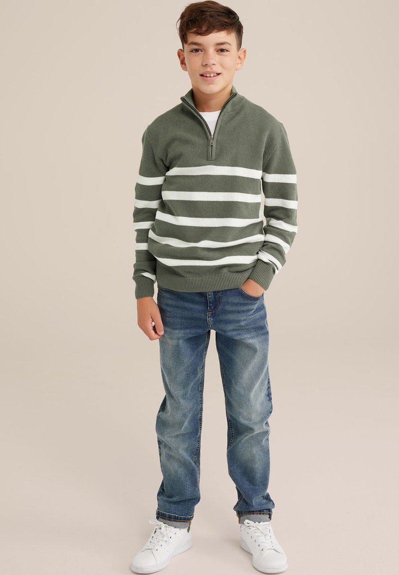 Grönrandig tröja med en kvartdragkedja, matchad med blå denimjeans och vita sneakers. Tröjan har horisontella vita ränder.