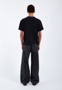 Camiseta de algodón negra de manga corta, combinada con jeans de mezclilla oscura de pierna ancha que presentan una textura desteñida y dos bolsillos traseros.