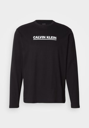 Czarna koszulka z długim rękawem wykonana z bawełny, z białym logo "CALVIN KLEIN" na wysokości klatki piersiowej. Okrągły dekolt i dopasowane rękawy.
