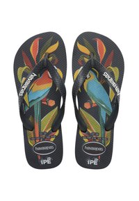 Tongs noires avec imprimé de feuilles tropicales et perroquets colorés, brides noires texturées et logo Havaianas sur les brides et les semelles.