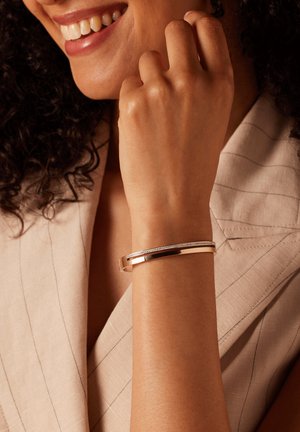 Metallarmband in Goldtönen mit einem schmalen Band, das eine Reihe kleiner klarer Steine entlang der Oberseite aufweist. Glatte Textur, modernes Design.