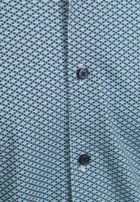 Korte mouwen shirt met een geometrisch blauw en wit patroon, gemaakt van een stof met een lichte textuur, met twee zwarte knopen aan de voorkant.