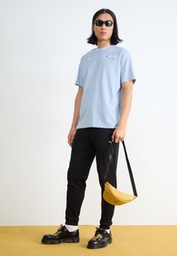 Light blue t-shirt with short sleeves, black sweatpants, black shoes with thick soles, and a small yellow shoulder bag.