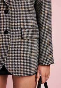 Ruda vilnos houndstooth bleizeris, rudos, jūros ir grietinėlės spalvų, su viena krūtine kišenė ir juodais mygtukais; tekstūruota medžiaga su pritaikytu kirpimu.