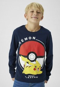 Hosszú ujjú, tengerészkék ing, amelyen egy nagy Pikachu grafika és egy Pokéball dizájn található, fehér és piros részletekkel az elején.