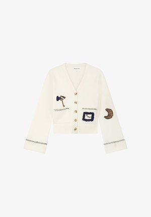 Weißer, kurz geschnittener Cardigan mit Knopfleiste, schwarz abgenähten Bündchen und Applikationen, darunter ein Schlüssel, ein eingerahmtes Etikett und ein Croissant an Ärmeln und Taschen.