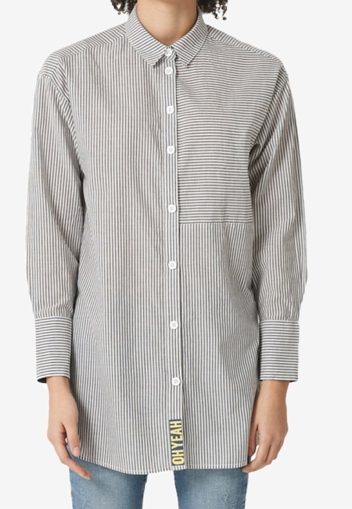 Chemise à manches longues boutonnée avec des rayures verticales noires et blanches et une poche rayée horizontalement sur la poitrine gauche, portée avec un jean bleu.
