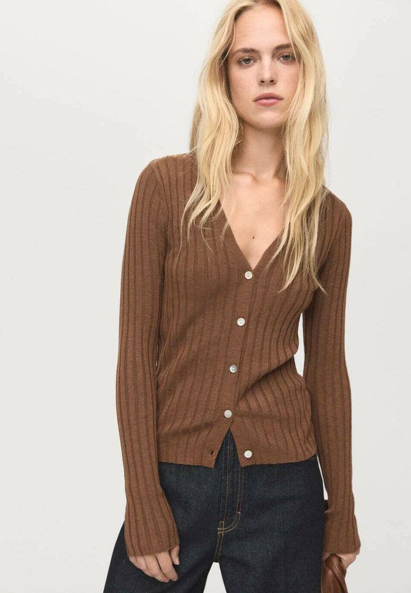 Cardigan marrone a coste con scollatura a V profonda, bottoni argento e maniche lunghe. Texture morbida e silhouette aderente. Indossato con jeans scuri.
