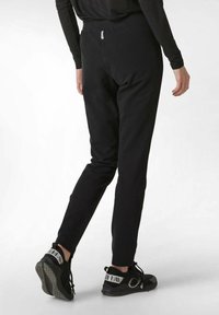 Schwarze Jogginghosen mit tailliertem Design, elastischem Bund und hinterer Reißverschlusstasche. Kombiniert mit schwarzen Sportschuhen mit kontrastierenden Akzenten.
