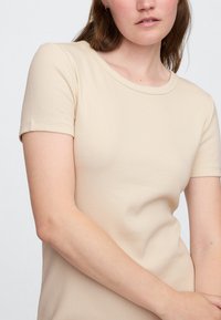 Beżowy prążkowany T-shirt z krótkimi rękawami i okrągłym dekoltem, wykonany z miękkiego, elastycznego materiału. Gładka tekstura i dopasowany krój.