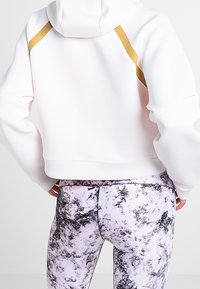 Hoodie blanc court avec des rayures dorées sur les épaules et des leggings taille haute à motif marbre en noir, blanc et violet clair.