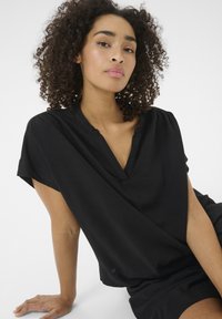 Schwarze, kurzärmlige Bluse mit V-Ausschnitt, hergestellt aus einem weichen Stoff. Hat drapierte Schultern und eine lockere Passform für zusätzlichen Komfort.