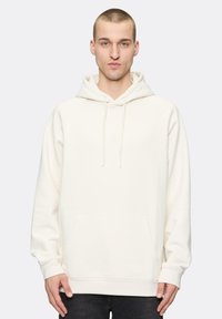 Kremowy hoodie z kieszenią kangurzą, kapturem na sznurku i rękawami raglanowymi. Miękka tekstura, minimalne logo na klatce piersiowej.