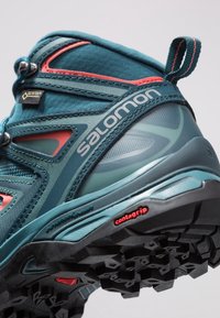 Tyrkysová turistická bota s šedými akcenty, s texturovaným svrškem, zesílenou špičkou a robustní černou gumovou podrážkou s označením "contagrip".