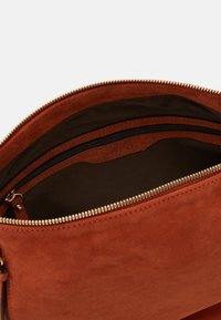 Ruskea mokkanahkainen laukun sisus, jossa on sileä pinta, vetoketjukiinnitys ja pieni lokero tummalla vuorauksella.