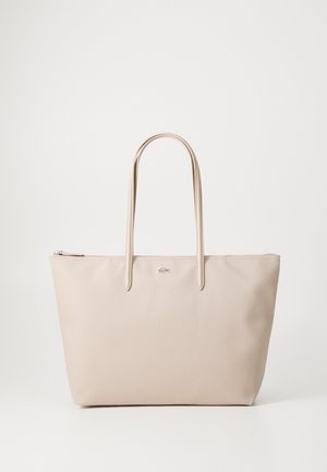 Beige tote bag made of textured material, featuring two elongated handles and a zip closure. Lacoste logo accent on the front.