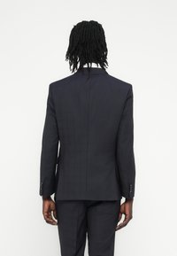 Tamsiai mėlynas švarkas su lieknu kirpimu, struktūruotais pečiais ir subtiliu languotu raštu. Turi vieną skeltuką ir užsegamus rankogalius.