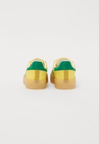 Sko med et gult og grønt fargevalg, med en glatt skinnoverdel og såle i beige gummi, designet med lav profil.