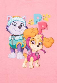 T-shirt rosa con cani dei cartoni animati. Un cane indossa un completo turchese con accenti bianchi; l'altro indossa un completo rosa con accenti viola.