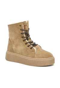 Botas de tobillo de gamuza color tan con suela de goma gruesa y estriada y cordones en color marrón negro, con un forro cálido y peludo y una marca roja en el cuello.