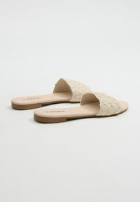 Sandalias planas con un upper tejido en beige, que presenta un diseño texturizado, punta abierta y una plantilla suave de color marrón claro.