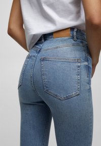 Jeans de mezclilla azul claro con una silueta ajustada, cinco bolsillos y un parche de cuero de marca en la cinturilla. Detalles de costura clásica.