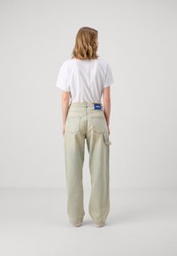 Ljusgröna, högmidjade byxor med baggy passform, synliga bakfickor och en etikett sydd på midjebandet. Vit t-shirt som bärs.