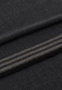 Sort stof med et fiskebensmønster og en kontrastfuld beige stribe. Teksturen er vævet med en blød finish, der viser subtile farvevariationer.