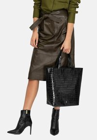 Czarna torba na ramię w kroku krokodyla z dwoma uchwytami, zestawiona z brązową skórzaną spódnicą i dopasowanymi czarnymi botkami za kostkę.