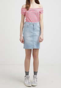 Světle modrá denimová sukně s rovnými liniemi, vysokým pasem a předními kapsami. V kombinaci s červeným a bílým pruhovaným topem bez raminek a teniskami.