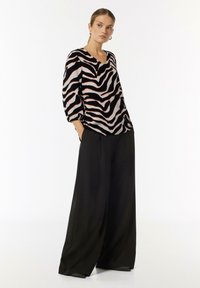 Schwarz-weiße Bluse im Zebra-Muster mit V-Ausschnitt und voluminösen Ärmeln, kombiniert mit weiten schwarzen Hosen. Glatte Stofftextur.