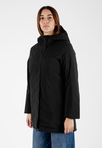 Giacca nera con cappuccio, zip frontale, tasche laterali e tessuto morbido. Presenta una vestibilità rilassata con maniche lunghe e un design minimale.