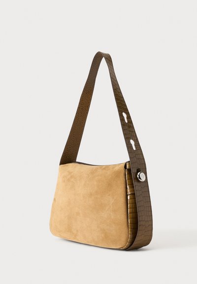 Petit sac à main en daim beige avec une large bandoulière texturée marron foncé comportant deux trous découpés et un bouton rond en argent.