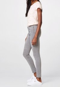 Jean skinny gris clair avec des détails aux genoux, associé à un haut rose à manches courtes avec un motif floral discret et des baskets blanches.