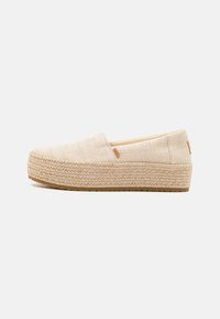 Scarpe beige senza lacci realizzate in tessuto intrecciato con una superficie testurizzata e una suola in giute intrecciato. Design minimalista con piccole rifiniture.