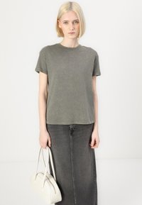 Olive green, short-sleeved t-shirt with a round neckline, relaxed fit, paired with a high-waisted, dark grey denim skirt and a cream handbag.