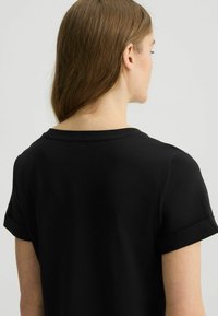 T-shirt nera con vestibilità comoda, maniche corte arrotolate e scollo rotondo. Texture liscia e design semplice senza loghi o motivi visibili.