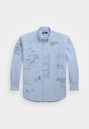 Camisa azul clara de botão com várias ilustrações impressas, incluindo texto e gráficos, com mangas longas e um bolso no peito.