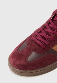 Burgunderfargede semskede sneakers med brune lærindlæg, med struktureret gummisål og flettede snøringer. Rund tå med kontrastfarvede accenter.