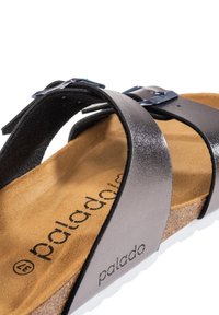 Sandal nera con due cinturini, dotata di fibbia metallica regolabile, sottopiede in sughero e suola in gomma bianca. Cinturini neri con texture e soletta con marchio.