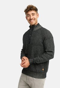 Strikket grå sweater med høj krave, der har en ribbet hals, tre knapper og en tekstureret stoffinish.