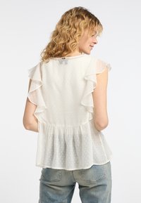 Weiße, leichte Bluse mit Punkten, Rüschenärmel und Peplum-Saum. Der Rücken hat einen Schlitzverschluss mit einem kleinen Akzent.