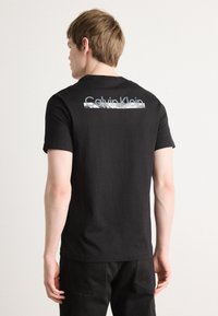 Melnā kokvilnas T-kreklā aizmugurē ir sudrabains logo prints. Vienkāršs apļa kakla dizains ar īsām piedurknēm. Gluda tekstūra.