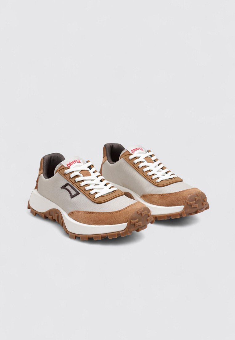 Lichtgrijze en bruine sneakers met witte veters, gestructureerde bovenkant, dikke zool en logo-accent aan de zijkant. Kenmerkt een mix van materialen.