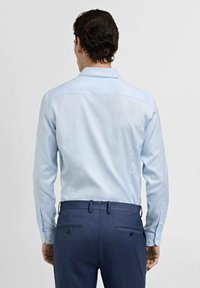 Cămașă albastră deschisă, cu guler structurat și mâneci lungi, asortată cu pantaloni albaștri închisi, având o textură netedă și o croială adaptată.