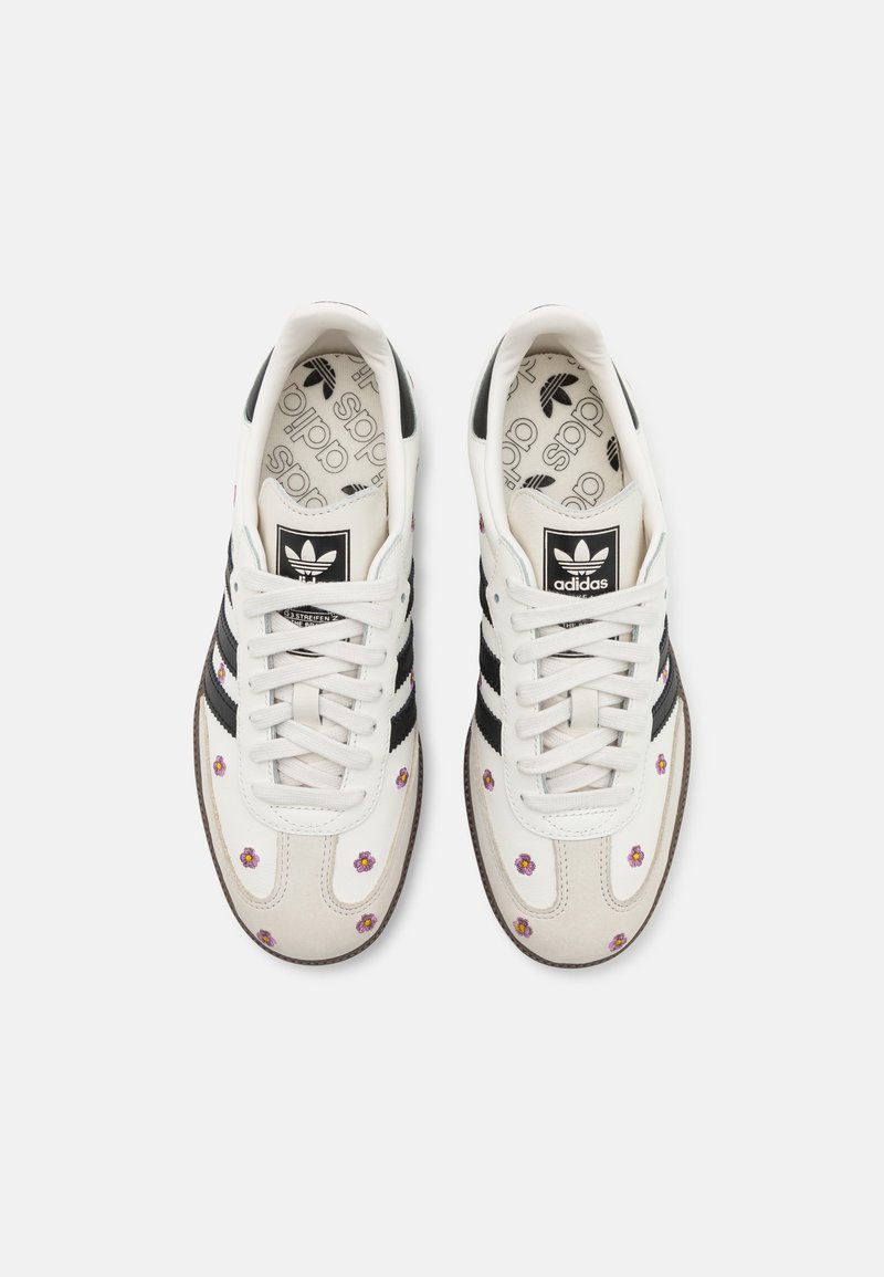 Sneakers bianchi e beige chiaro con strisce nere, ricami floreali e suola in gomma. Design a punta rotonda e lacci con tessuto in canvas.